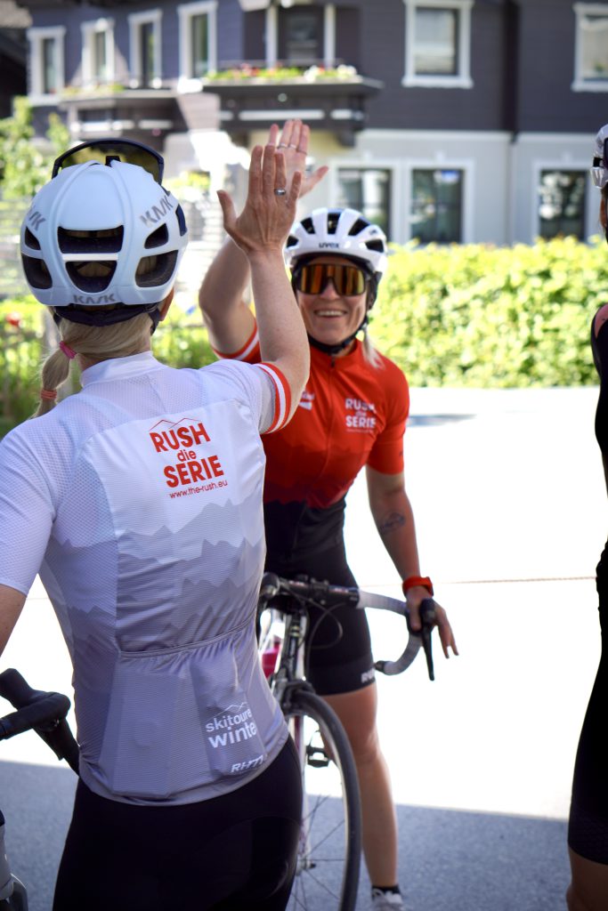 Rennradfahrende Frauen in bunter Sportkleidung fahren gemeinsam durch grüne Alpenlandschaft