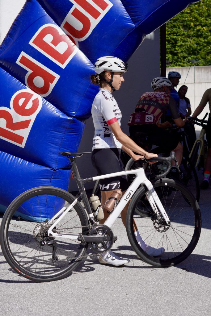 Rennradfahrende Frauen in bunter Sportkleidung fahren gemeinsam durch grüne Alpenlandschaft